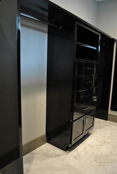Black, glossy closet with hanging rod, shelves, drawers, and cabinet, set against light-colored floor.