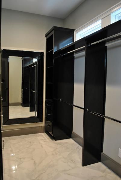 Black custom closet with hanging rods, shelving, and full-length mirror, set against a white tile floor.