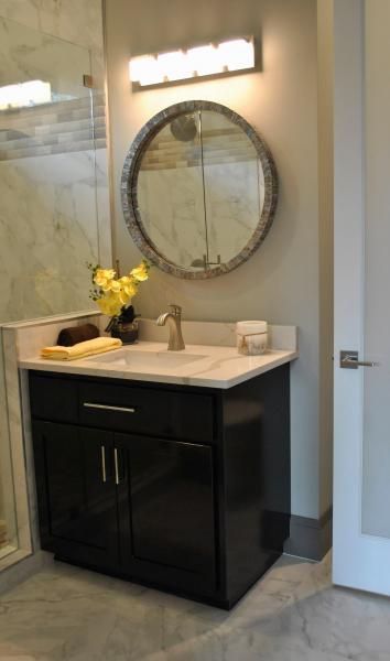 Bathroom vanity with a round mirror, black cabinet, and white countertop. A floral arrangement and soap dish are displayed.