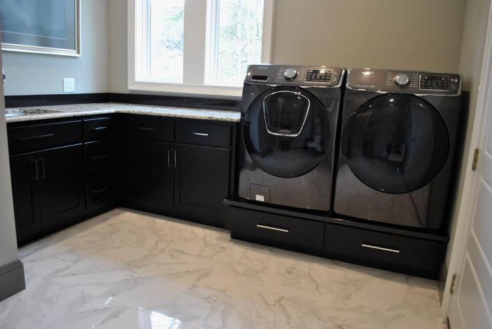 Laundry room with black cabinets, washer and dryer. White and gray countertop and flooring.