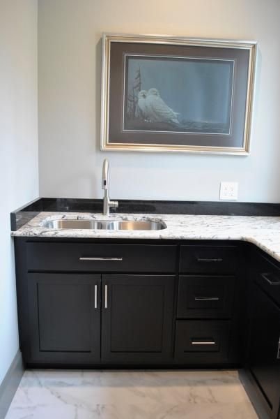 Black cabinets with a sink, granite countertop, and framed art.