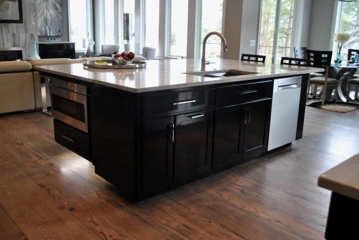 Dark kitchen island with sink, dishwasher, and cabinetry on hardwood floor.