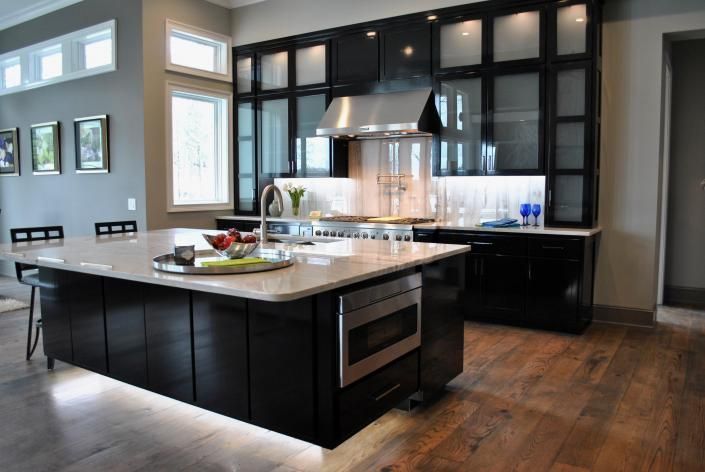 Modern kitchen with dark cabinetry, stainless steel appliances, and large island with under-cabinet lighting.