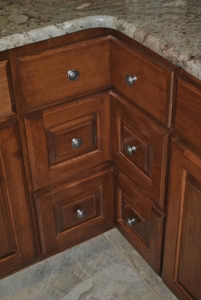 Corner kitchen cabinets with brown wooden doors and silver knobs under a granite countertop.