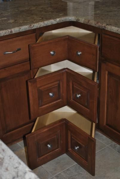 Brown corner kitchen cabinet with three pull-out drawers. Light-colored countertop and floor.