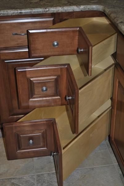 Open kitchen drawers in a corner cabinet; brown wood with light-colored interiors and silver knobs.
