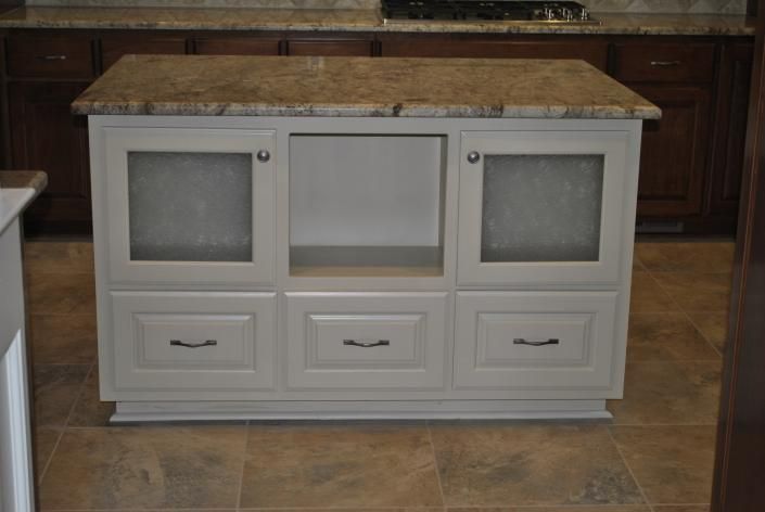 Kitchen island with light gray cabinets, granite countertop, and frosted glass doors.