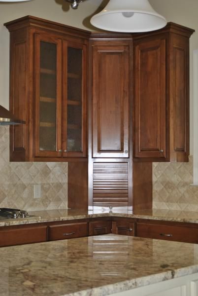 Corner kitchen cabinets with glass doors, brown wood, granite countertop, and pendant light.