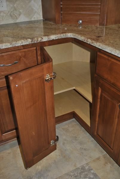 Open corner kitchen cabinet with shelves, brown wood, and granite countertop.