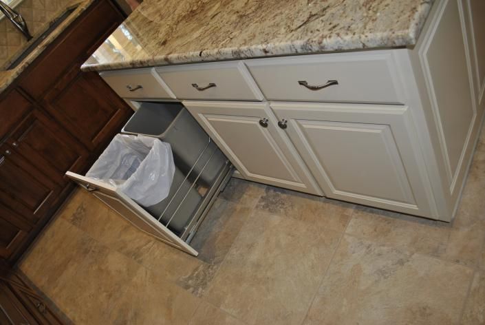 Kitchen cabinet with a pull-out trash can; a countertop, and a tiled floor.