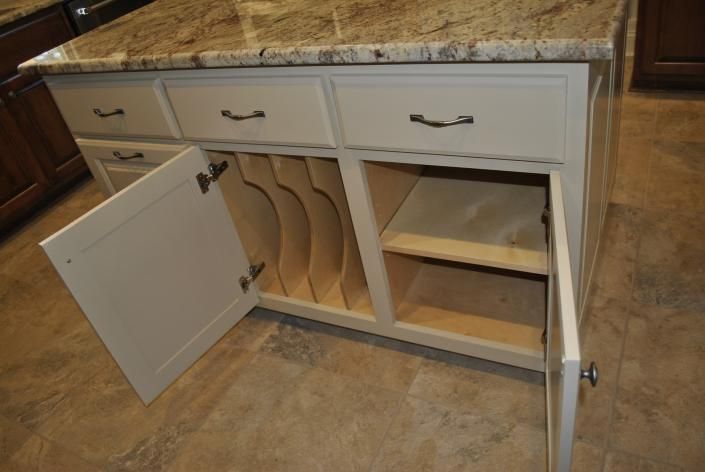 Kitchen island with cream cabinets, granite countertop, open doors, and storage for cutting boards.