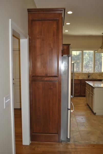 Tall, dark wood cabinet next to a stainless steel refrigerator in a kitchen.