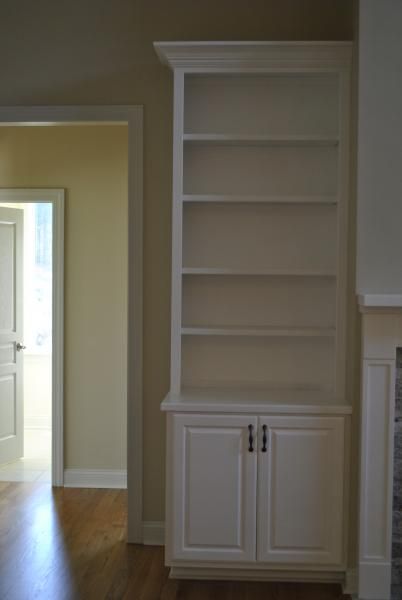 White built-in bookcase with shelves and cabinet doors; beside a doorway and fireplace.