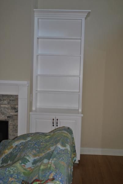 White built-in bookshelf with shelves above a cabinet. The unit is against a tan wall, next to a fireplace.