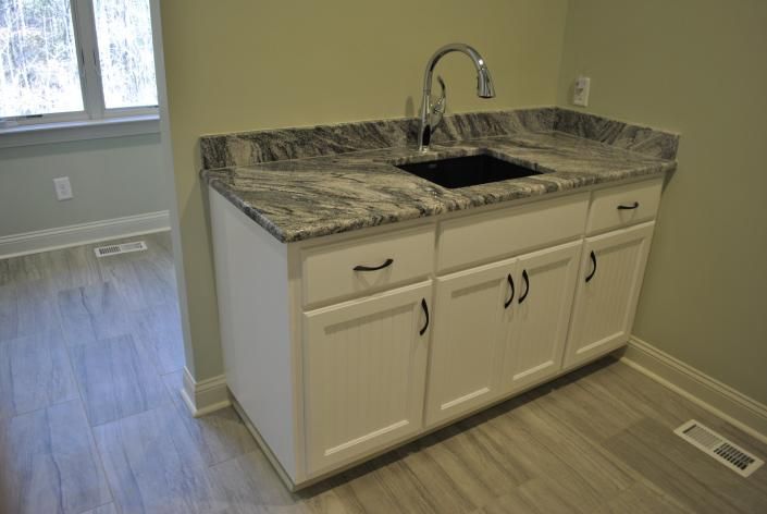 White cabinet with granite countertop and black sink; chrome faucet.