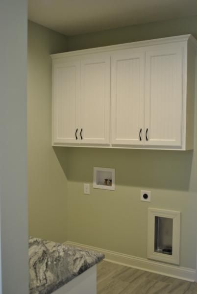 White cabinets over laundry hookups in a room with light green walls.
