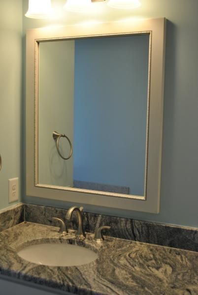 Bathroom mirror above a sink with granite countertop and light blue wall.