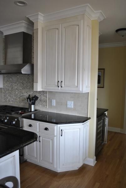 White kitchen cabinets with black countertops, next to a stainless steel range hood and a yellow wall.