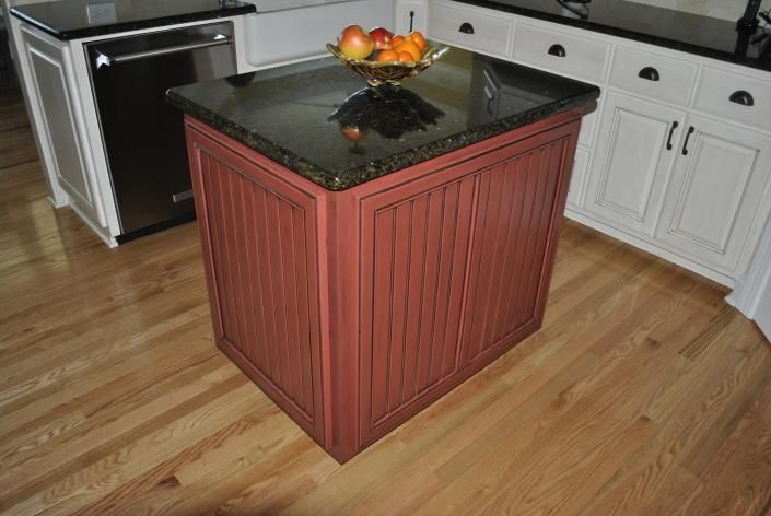 Kitchen island with reddish-brown paneled sides, black granite countertop, and fruit bowl; wood floor.