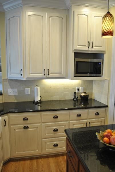 Cream-colored kitchen cabinets with black countertops. Microwave above lower cabinets, hardware is dark.
