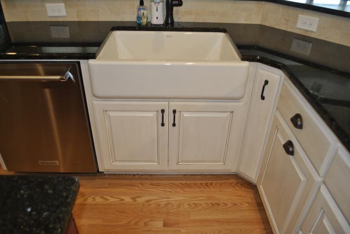 Kitchen sink and cabinets with stainless steel dishwasher and black countertops.