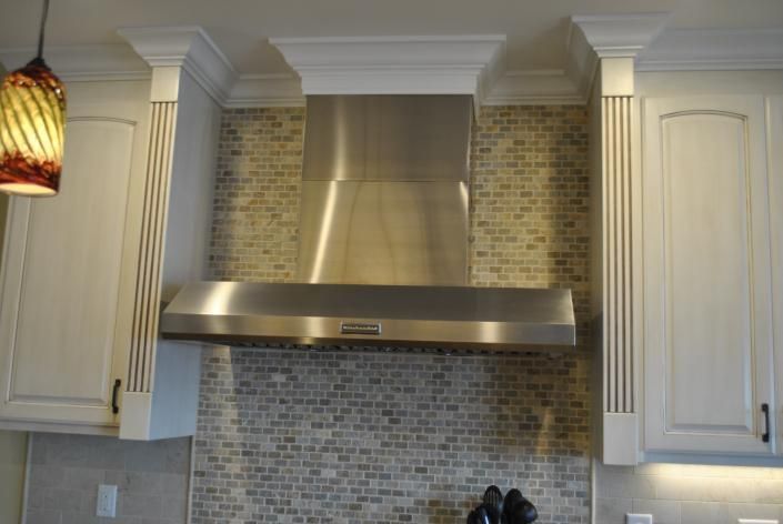 Stainless steel range hood centered on a mosaic tiled backsplash, flanked by white cabinets.