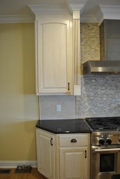 Kitchen cabinets: cream-colored, with black countertop and stainless steel stove. Yellow wall, mosaic backsplash.