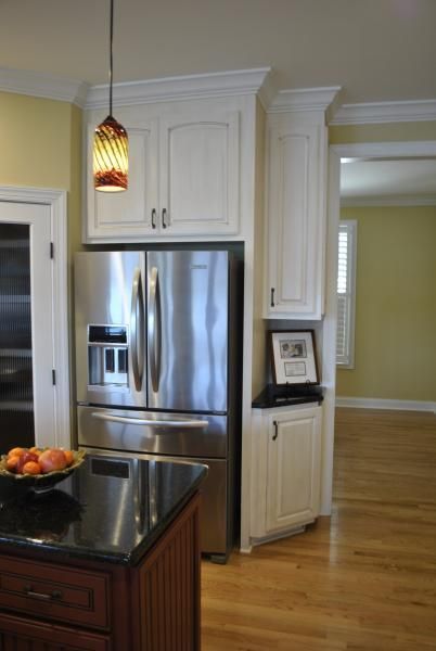 Stainless steel refrigerator and white cabinets in a kitchen, with a hanging light fixture and a granite countertop.