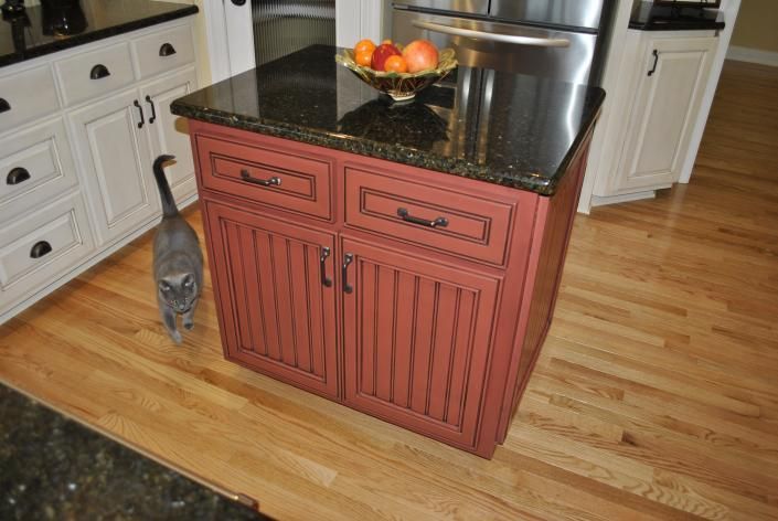Kitchen island with a granite countertop, red cabinet, and a cat.