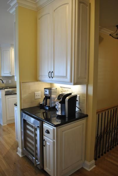 White cabinets house coffee maker, Keurig, and wine cooler on black countertop.