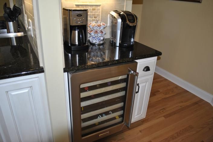 Built-in wine cooler with door open, counter with coffee maker, Keurig, and cabinet.
