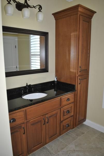 Bathroom with wooden vanity, dark countertop, and tall cabinet.