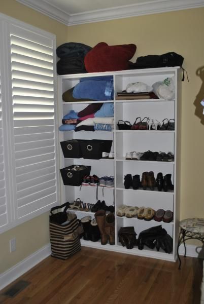 White shelving unit filled with shoes and storage items against a yellow wall and wood floor.