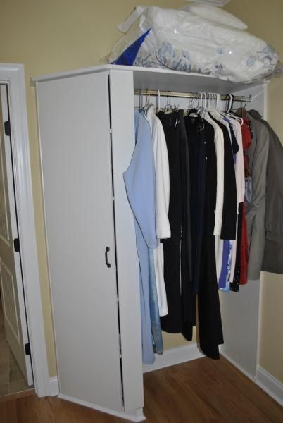 White closet with hanging clothes; towels on top. Door and beige walls visible.