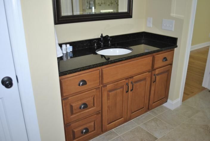 Bathroom vanity with dark countertop, brown cabinets, and black faucet.