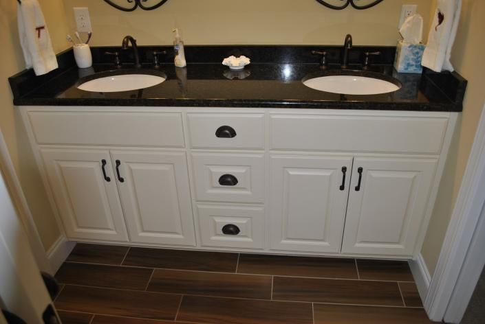 White double vanity with black countertop, sinks, and hardware. Brown tile floor.