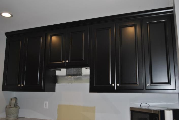 Black kitchen cabinets with brushed silver handles against a white wall.