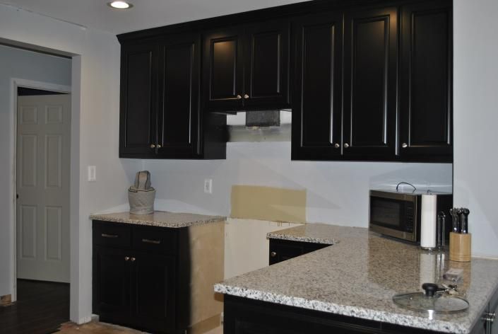 Black kitchen cabinets with granite countertops. A microwave and decorative items sit on the counter.