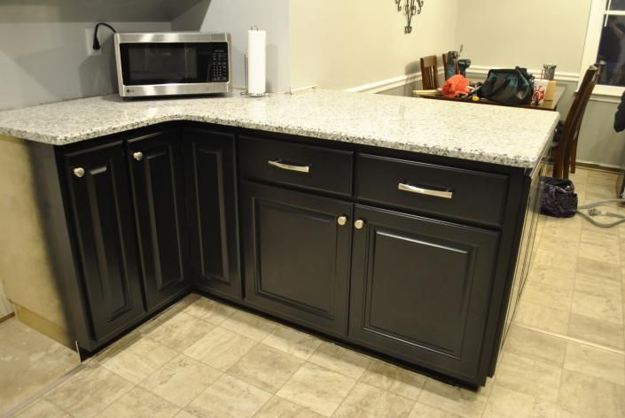 Black kitchen cabinets with granite countertop, microwave, and paper towel holder.