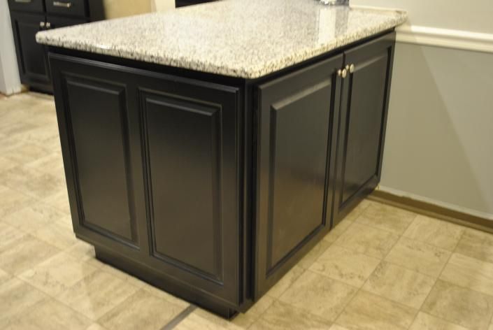 Black kitchen island with granite countertop. Cabinet doors and floor visible.
