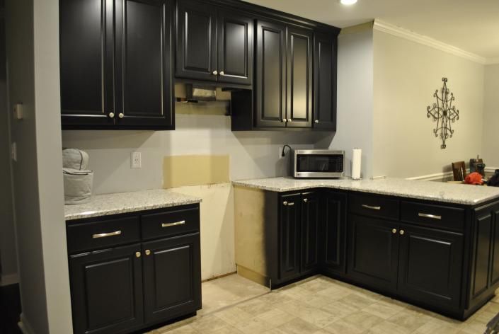 Black kitchen cabinets with granite countertops. A microwave sits on the counter.