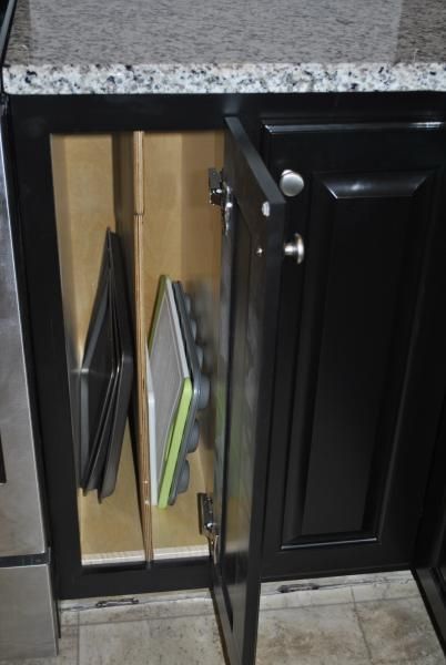 Open kitchen cabinet with baking pans stored vertically.