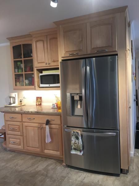 Kitchen with light wood cabinets, stainless steel refrigerator, and countertop with microwave.