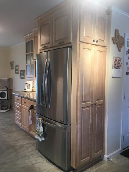 Stainless steel refrigerator surrounded by light wood kitchen cabinets; a Texas-shaped wooden decoration hangs on the wall.
