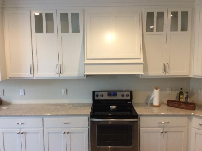 White kitchen cabinets with range, range hood, and light-colored countertops.