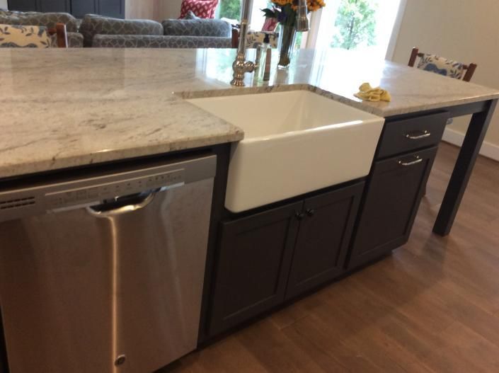 Kitchen island with stainless steel dishwasher, farmhouse sink, and dark brown cabinets. Beige countertop.