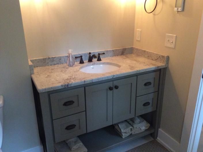 Gray bathroom vanity with granite countertop, white sink, and black faucet.