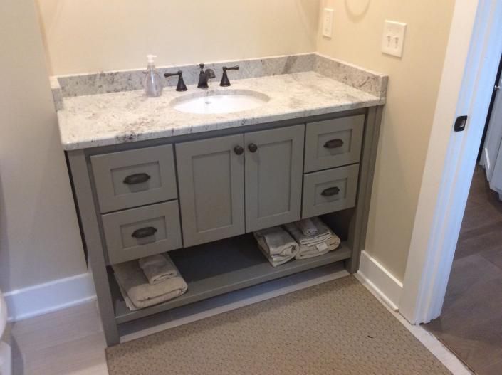 Gray bathroom vanity with granite countertop, dark faucet, and cabinet storage.
