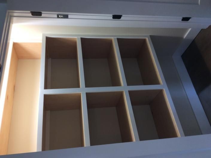 Open white cabinet interior with six square compartments and one long, rectangular space.