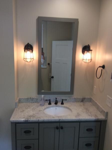 Bathroom vanity with a gray cabinet, marble countertop, and a mirror. Two sconce lights flank the mirror.